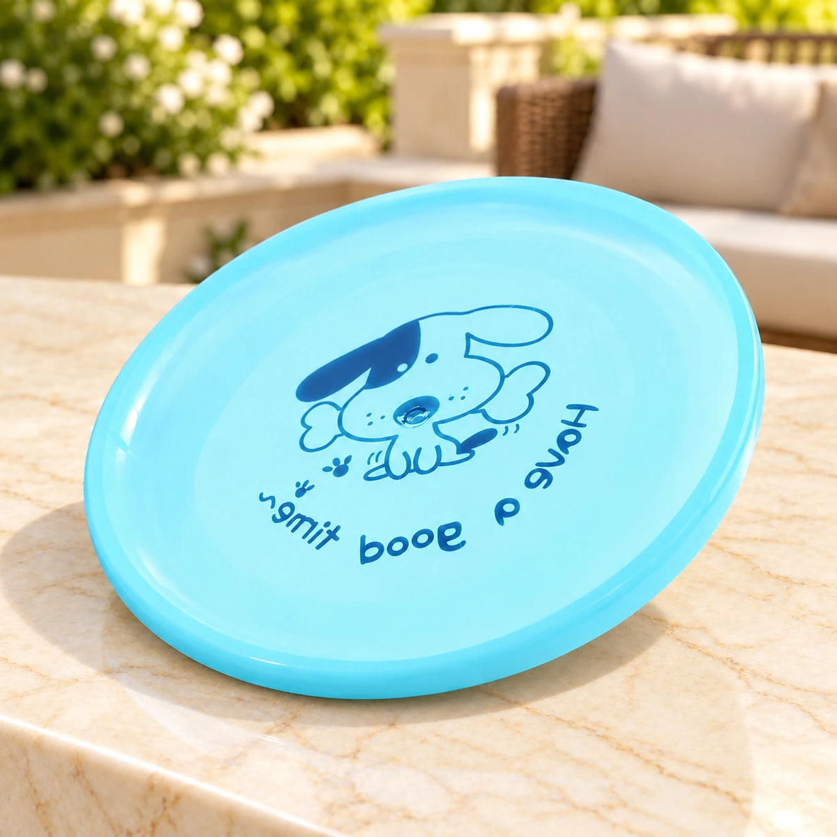 Light blue dog flying disc with the original dog-and-bone print on a light ivory-beige marble terrace table.