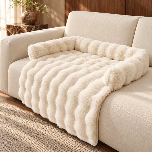 Cream plush dog sofa mat with raised bolsters and a draped front on a cream fabric sofa.