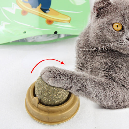 Gray cat pawing at catnip ball toy in brown base with arrow showing rotary motion