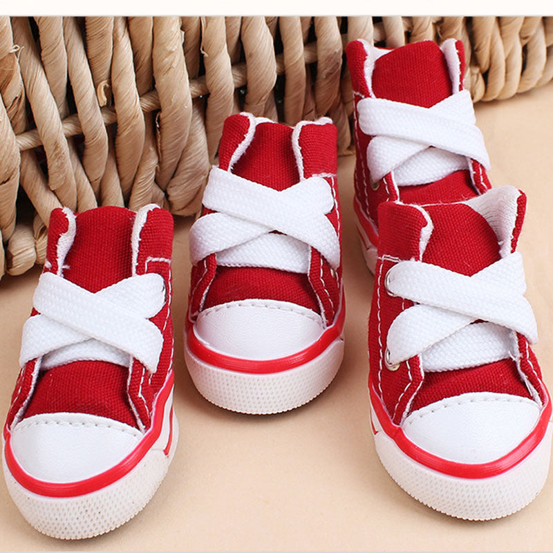 Group of red mini canvas dog sneakers with white laces arranged on neutral surface
