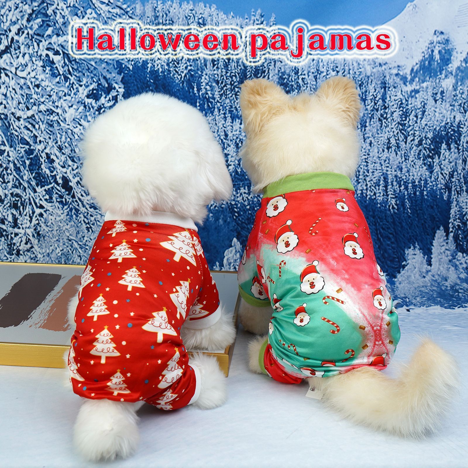 Two small dogs wearing colorful festive holiday pajamas sitting side by side facing a snowy winter backdrop, one with red pajamas featuring Christmas trees and the other with green and red pajamas decorated with Santa faces and candy canes