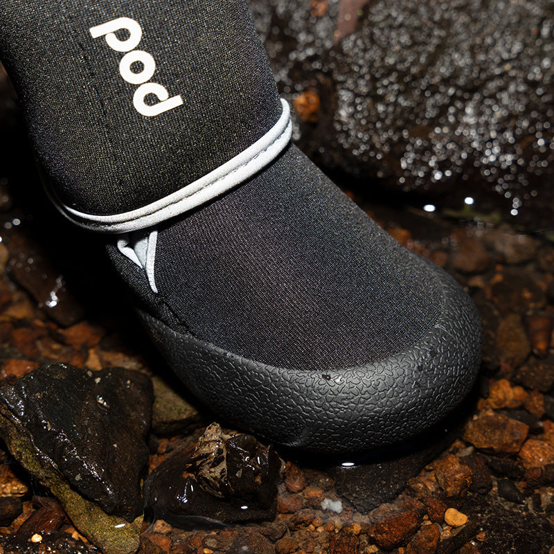 Detailed close-up of black waterproof dog boot covering paw surrounded by wet stones