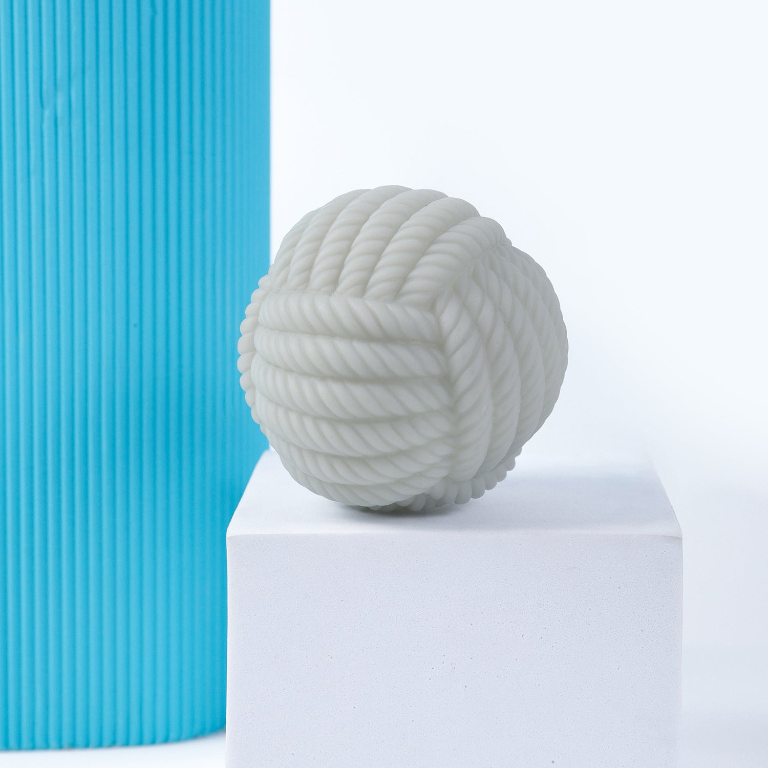 White rope-textured ball dog toy positioned on a white pedestal with blue background