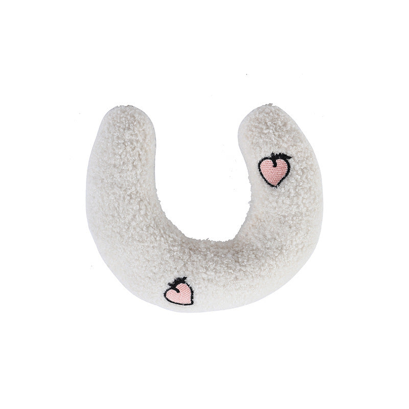 White crescent plush pet pillow with pink embroidered hearts on plain background