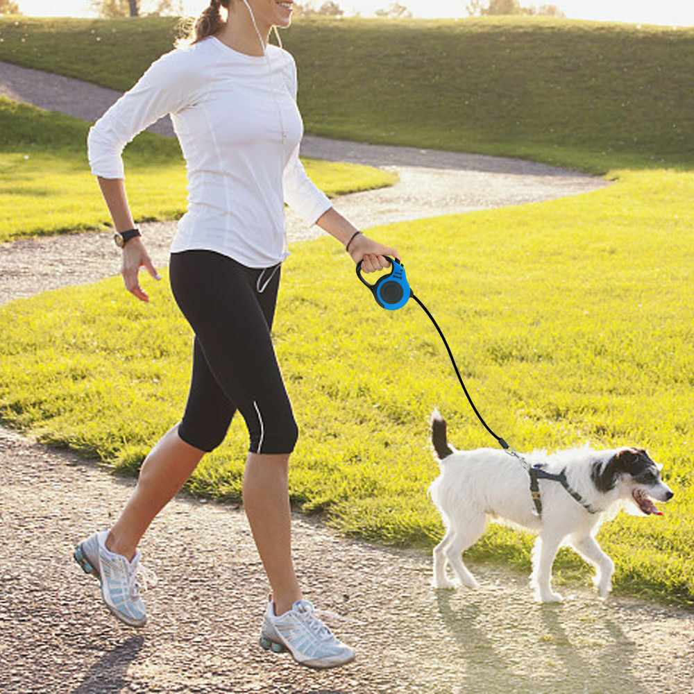 Woman jogging outdoors holding blue retractable leash walking a medium-sized white dog with black and brown spots