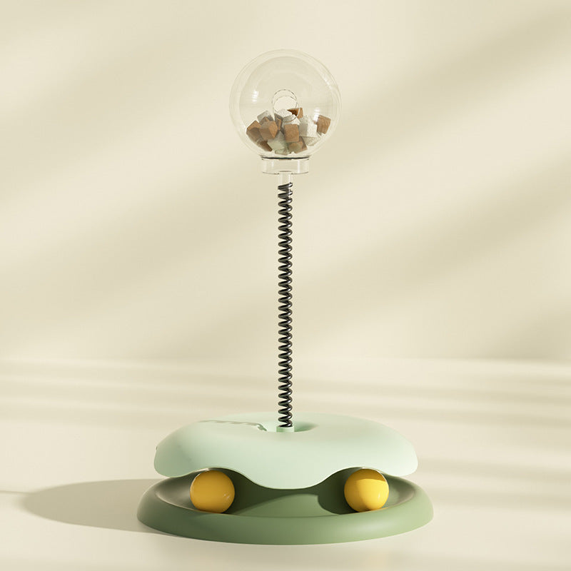 Green interactive cat treat toy with clear treat container and spring stem on soft beige background