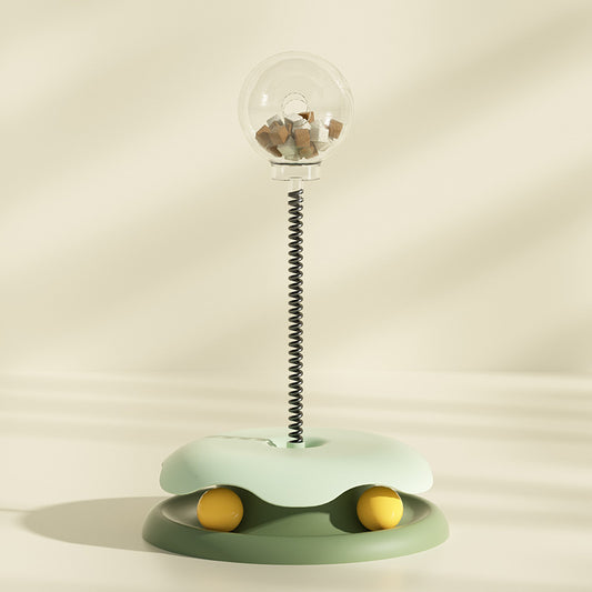 Green interactive cat treat toy with clear treat container and spring stem on soft beige background
