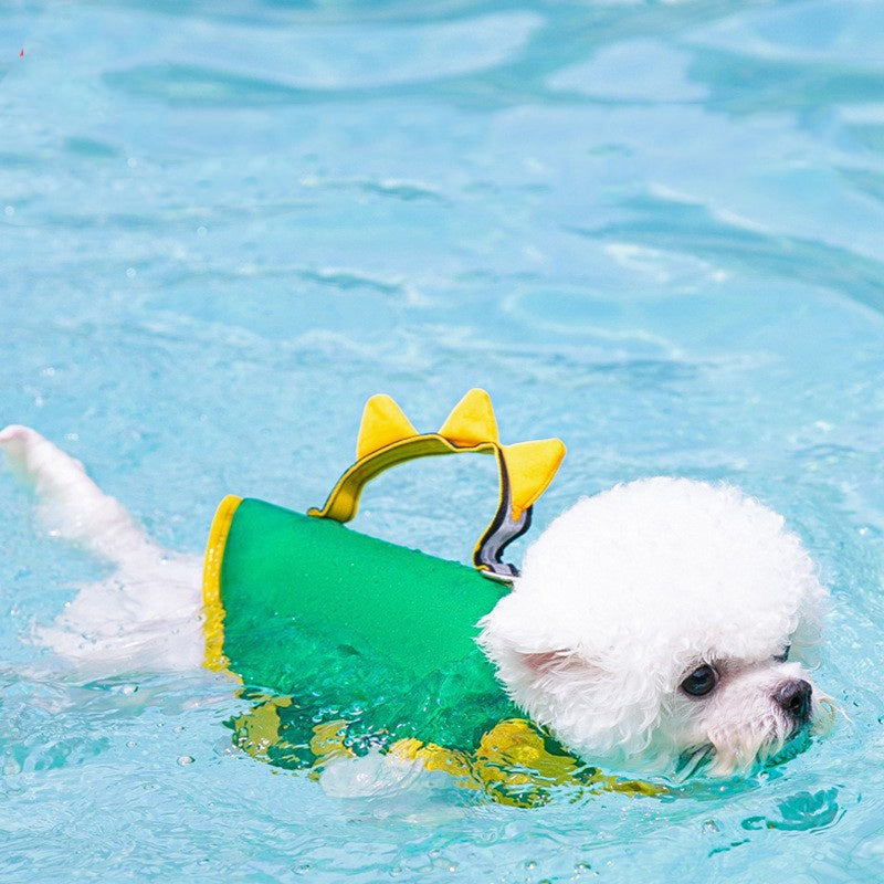 Small white dog swimming in pool wearing a green and yellow dog life vest with triangle fin accents on back