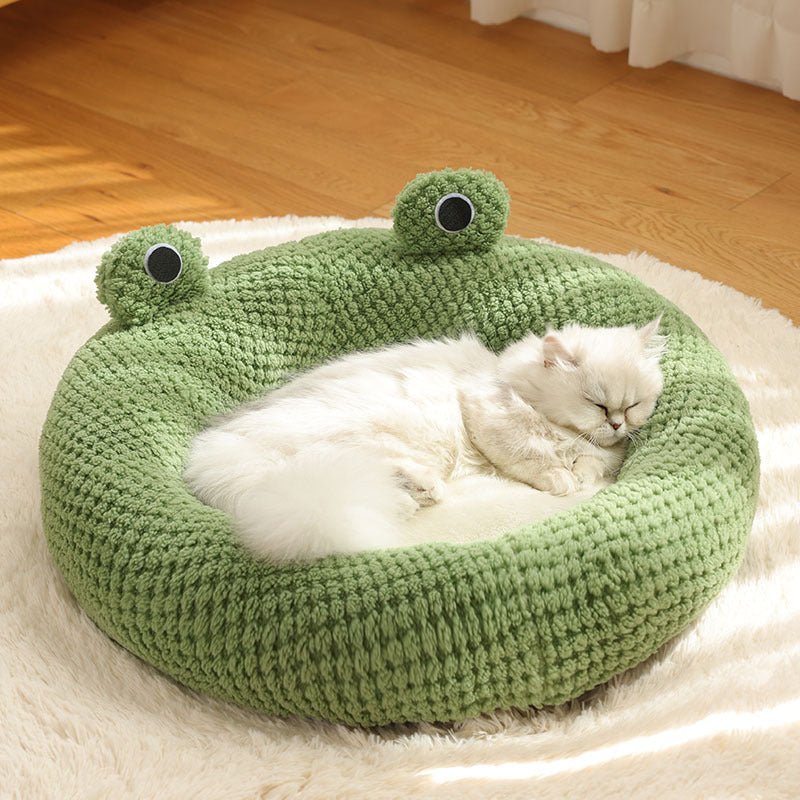 Green knitted frog-shaped pet bed with cat peacefully sleeping inside on a soft rug