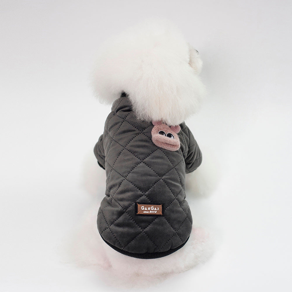 Small white fluffy dog wearing charcoal gray quilted jacket with embroidered pink animal patch on back
