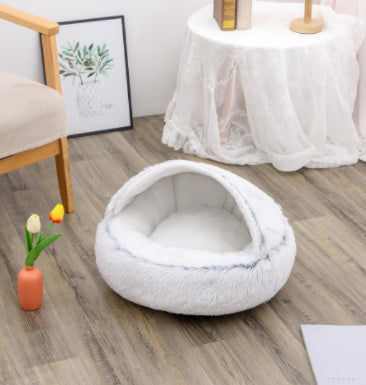 Gray plush dome pet bed on wooden floor next to white table covered with lace