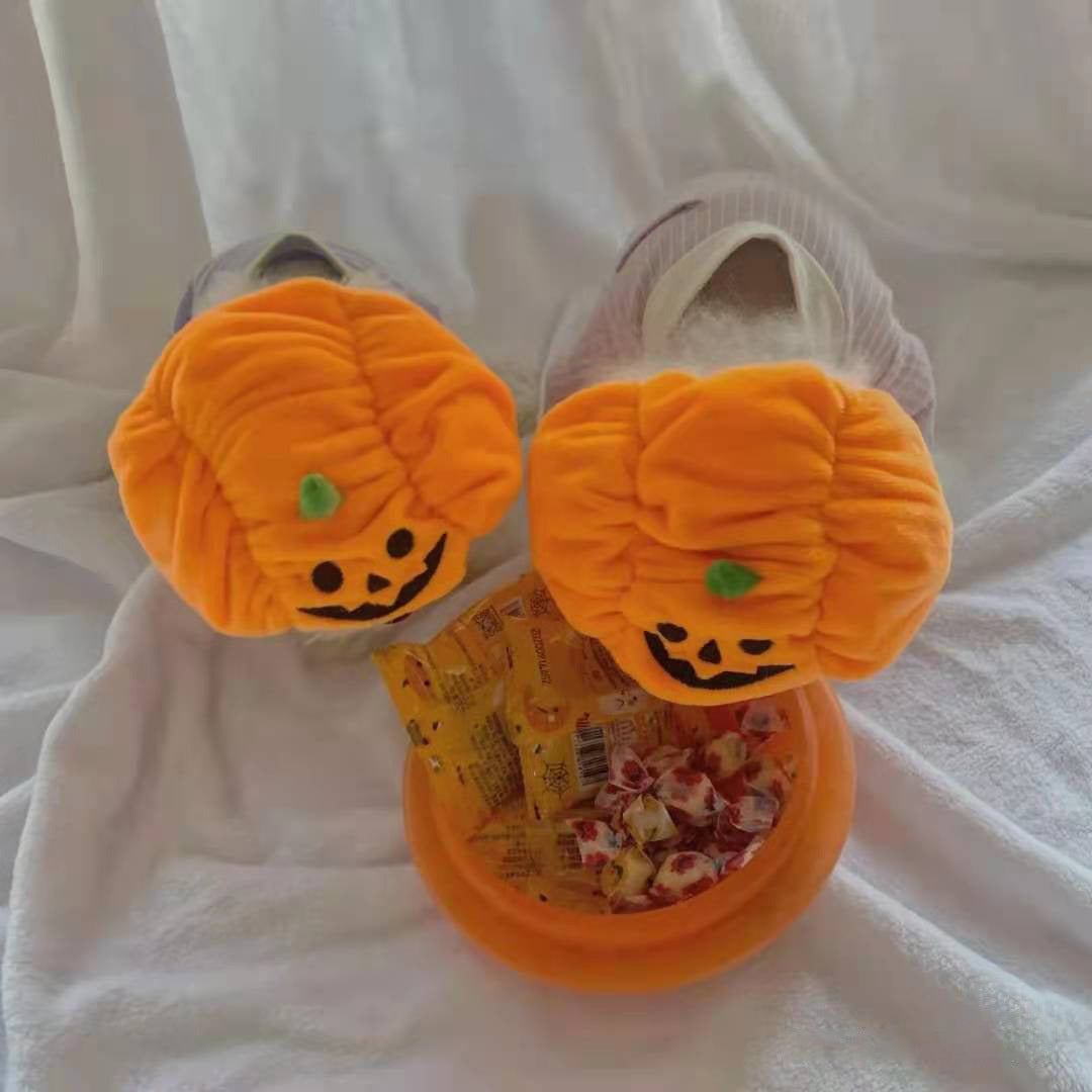 Two small dogs viewed from above wearing plush pumpkin hats near a bowl of wrapped candy