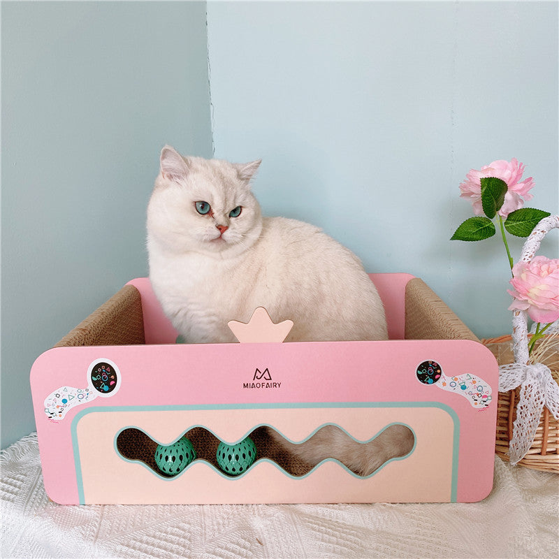 White cat sitting inside pink crown-shaped corrugated cat scratcher bed next to flowers