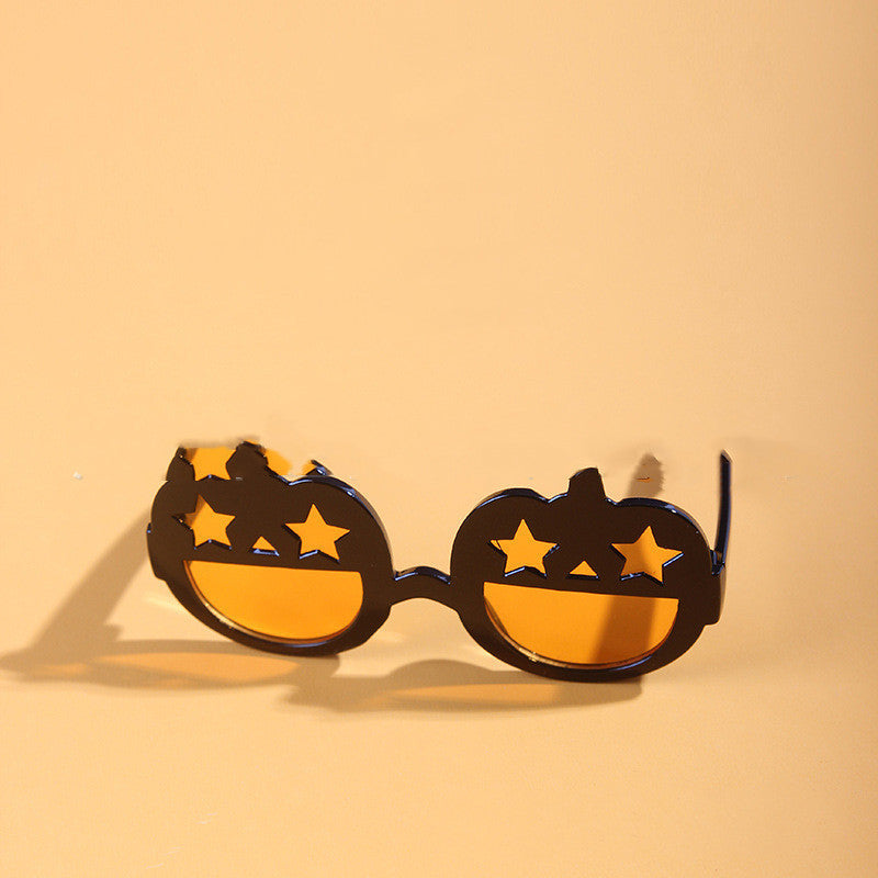 Orange and black pumpkin-shaped pet sunglasses with star-shaped eye holes displayed on beige background