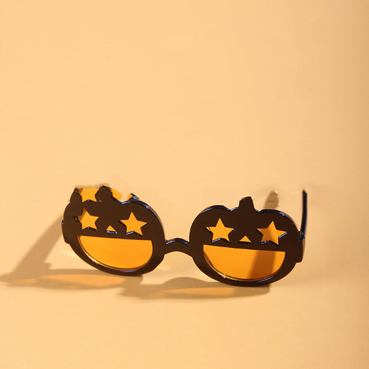 Orange and black pumpkin-shaped pet sunglasses with star-shaped eye holes displayed on beige background
