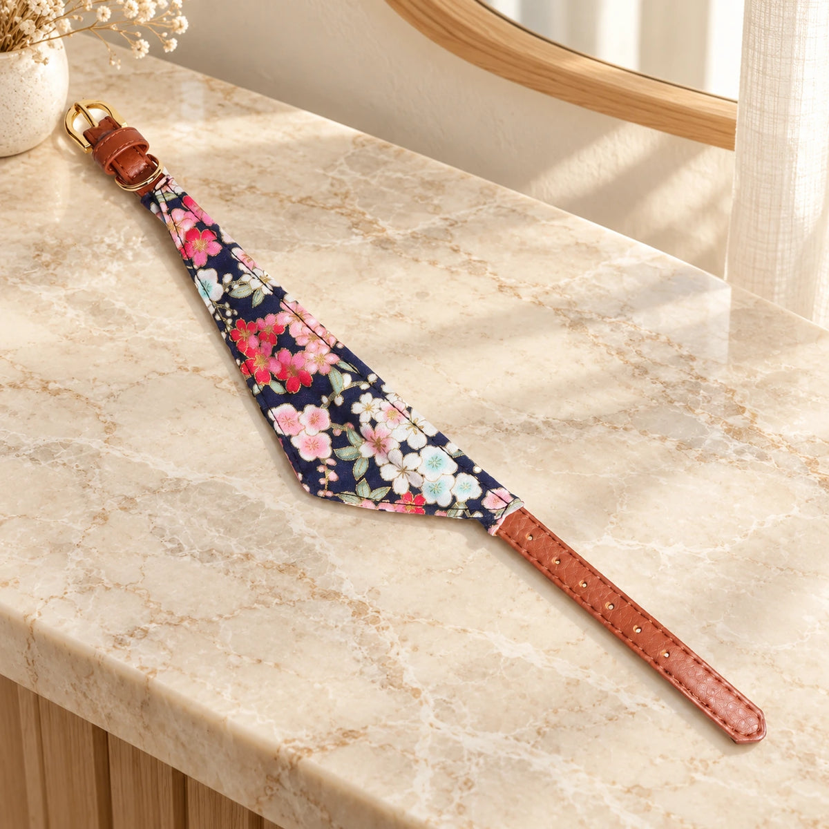 Navy floral scarf collar with brown straps and gold-tone buckle on beige marble