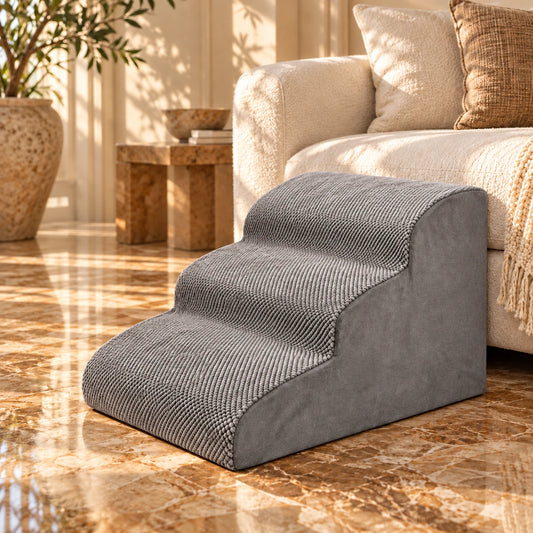 Grey three-step foam pet stairs beside a cream sofa on warm brown veined stone.