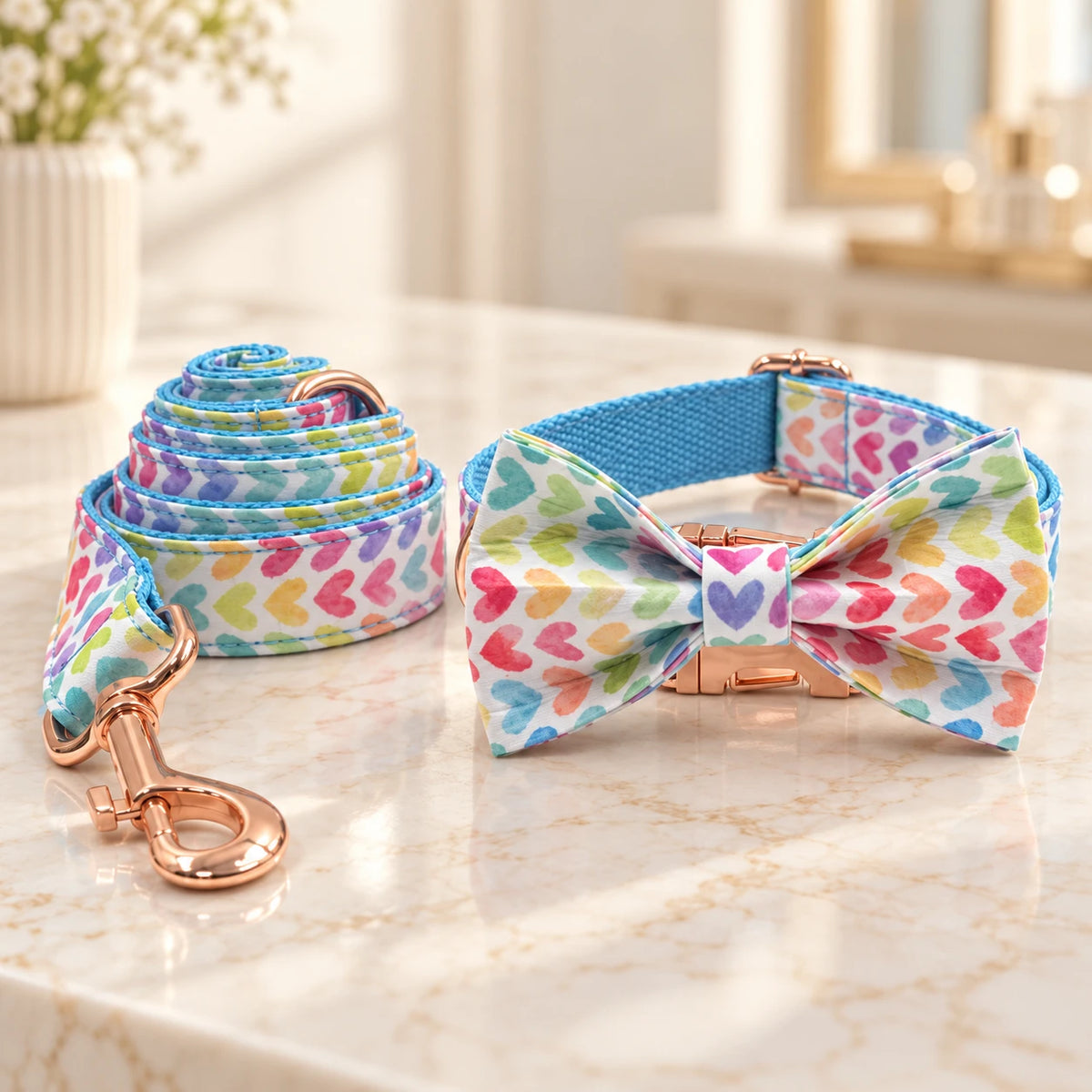 Multicolour heart-print dog collar with bow and matching leash with rose-gold hardware on an ivory marble console