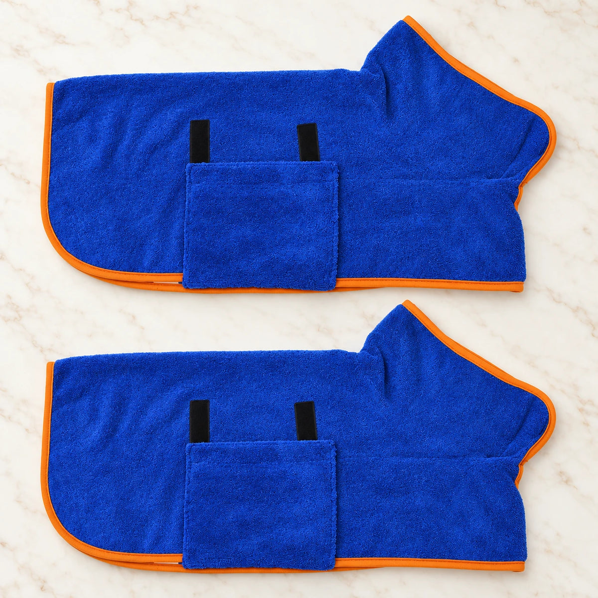 Two royal blue dog drying robes with orange trim on ivory marble