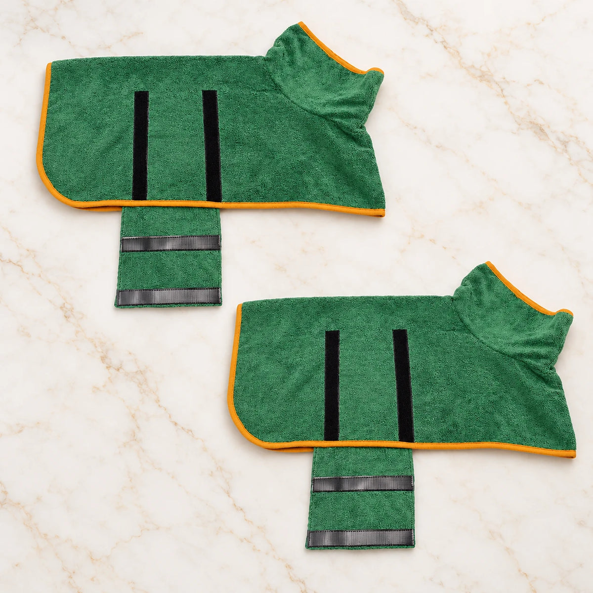 Two green dog drying robes with orange trim and open fastening flaps on ivory marble