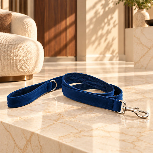 Navy velvet dog leash with silver snap clasp and loop handle on light ivory-beige marble in a sunlit interior.