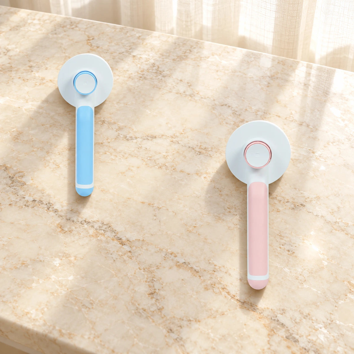 Blue and pink round-head grooming brushes showing rear buttons on beige marble