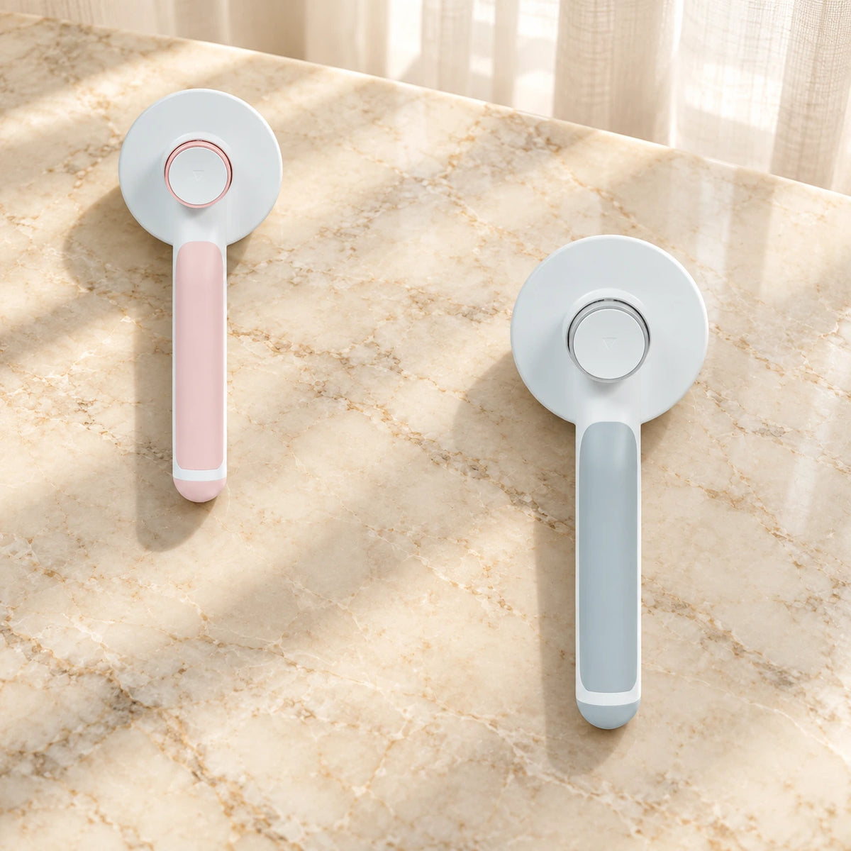 Pink and grey round-head grooming brushes showing rear buttons on beige marble